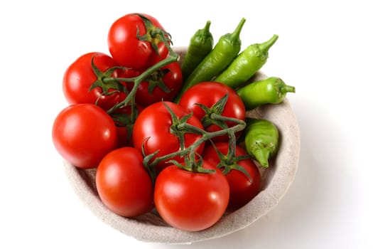 Red tomatoes an green peperoni in basket on white background