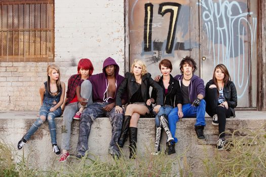 Bunch of punk teens look to the camera with serious expressions behind an abandoned building.