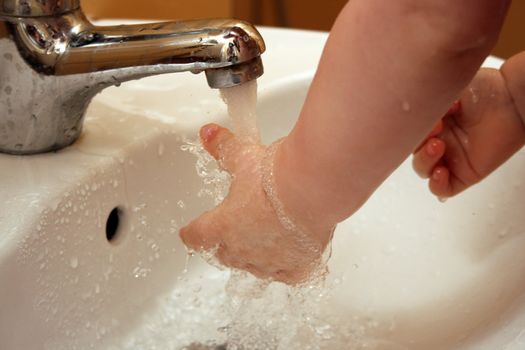 Baby wash her hands in white ceramic sink with splashing water