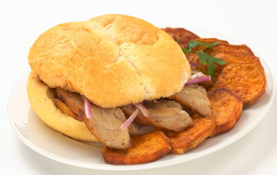 Peruvian sandwich called Pan con Chicharron which is traditionally eaten for breakfast, and is prepared with fried pork and sweet potato and filled with ketchup and onions and served with fried sweet potato (Selective Focus, Focus on the front of the bun and the two meat slices on the right) 