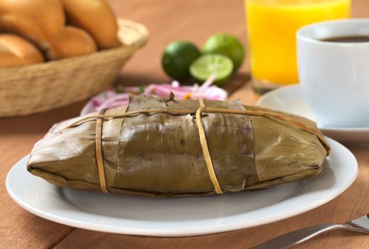 Peruvian food called Tamal which is prepared from cooked corn mixed with chicken meat and wrapped in banana leaves. It is eaten for breakfast or as appetizer at lunchtime (Selective Focus, Focus on the front of the tamal)