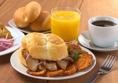 Typical Peruvian breakfast consisting of Pan con Chicharron (Bun with fried meat) and fried sweet potato, tamal (on the left), salsa criolla (onion salad) with coffee, orange juice and buns (Selective Focus, Focus on the front)