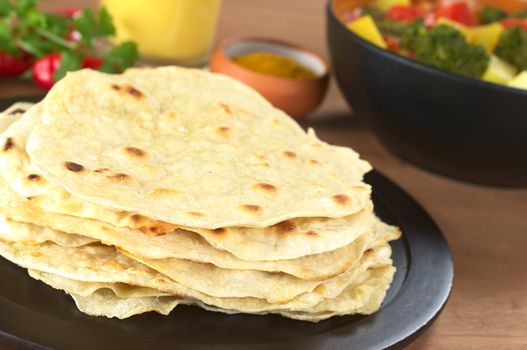 Indian flatbread called Chapati with vegetable curry, curry and mango lassi in the back (Selective Focus, Focus on the front of the chapati) 