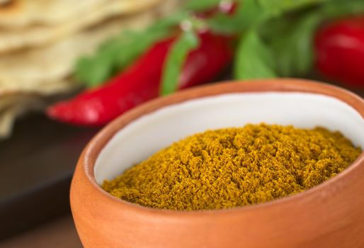 Curry spice in small bowl with chapati, hot pepper, and cilantro in the back (Selective Focus, Focus in the middle of the bowl)