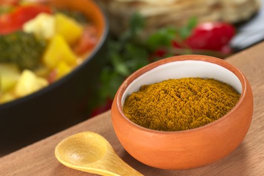 Curry spice in small bowl with a small spoon beside it and vegetable curry and chapati in the back (Selective Focus, Focus in the middle of the bowl)