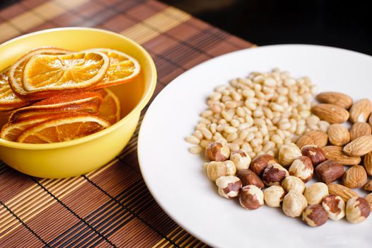 Mixed nuts on a white plate and dried orange