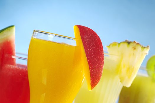 Mango, melon, pineapple and kiwi smoothies garnished with the corresponding fruit on the rim on blue background (Selective Focus, Focus on the mango smoothie in the front) 