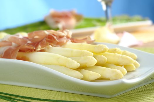 Fresh cooked white asparagus served with ham with white wine and green asparagus in the background (Selective Focus, Focus on the front of the asparagus on the left)