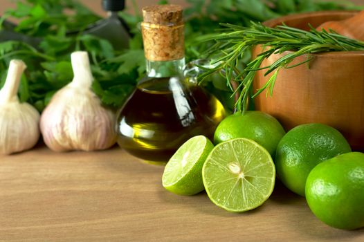 Limes and other seasonings such as rosemary, olive oil, garlic and parsley with mortar on wooden board (Selective Focus, Focus on the half lime and some of the rosemary twigs)