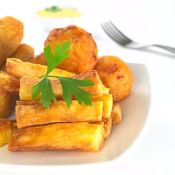 Fried manioc sticks garnished with parsley with fork and dip in the back (Selective Focus, Focus on the sticks and the parsley)