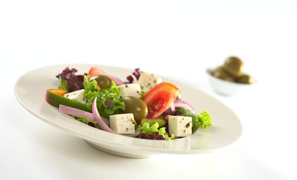 Greek salad out of white cheese, olives, red onions, tomato, bell pepper, cucumber and lettuce with herbs with some olives in bowl in the back (Selective Focus, Focus on the front of the salad) 