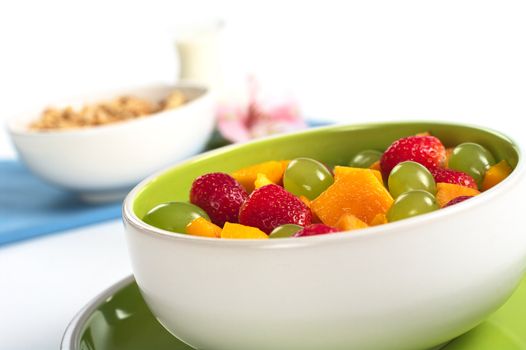 Fresh fruit salad of strawberries, white grapes and mango with cereals, milk and a flower in the back (Selective Focus, Focus on the front)