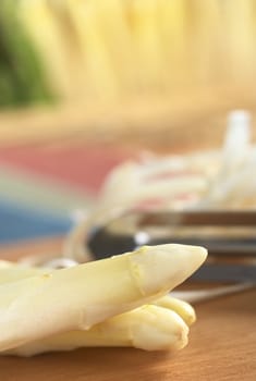 Two white asparagus with peeler and asparagus peel in the back on wooden board (Very Shallow Depth of Field, Focus on the two asparagus heads)