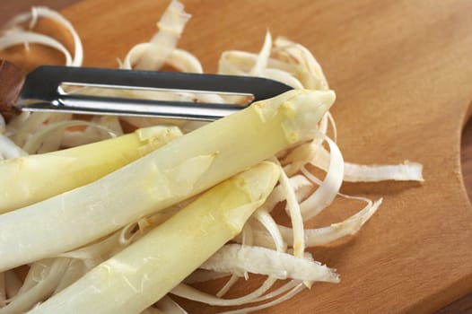 Peeling white asparagus on a wooden cutting board (Selective Focus, Focus on the head of the asparagus on the top) 