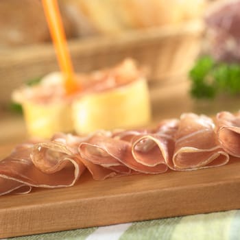 Thin ham slices on wooden cutting board with sandwich in the back (Very Shallow Depth of Field, Focus on the front of the slices)