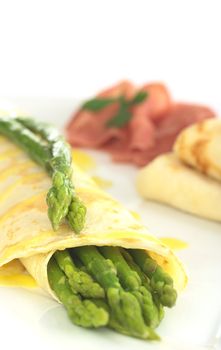 Green asparagus wrapped in crepes with Hollandaise sauce and green asparagus as garnish on top (Selective Focus, Focus on the asparagus heads on top of the crepes)