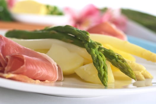 Green asparagus on cooked potato pieces with ham slices in front (Selective Focus, Focus on the asparagus head in front and the tip of the second)