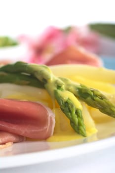 Green asparagus on cooked potato pieces with Hollandaise sauce on top and ham slices in front (Selective Focus, Focus on the asparagus head)