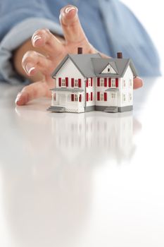 Womans Hand Reaching for Model House on a White Surface.