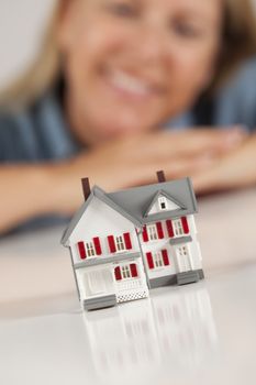 Smiling Woman Leaning on Hands Behind Model House on a White Surface.