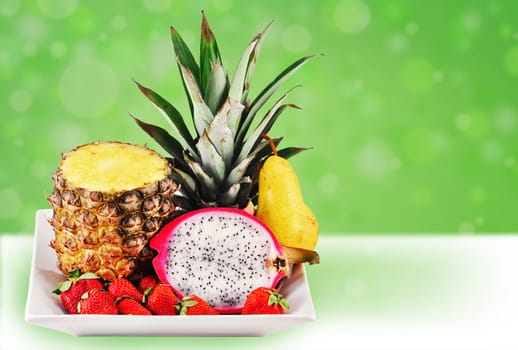 Welcome to the tropics: tropical fresh fruits served in a white plate on fun green background.
