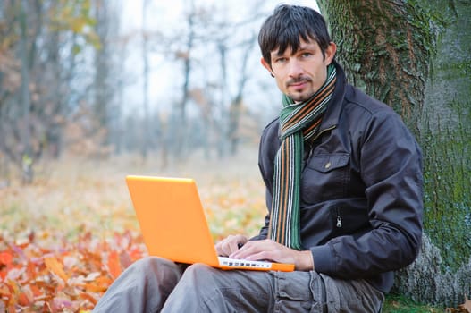 Romantic young man sitting with laptop in the autumn park.