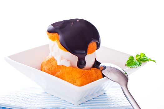 Profiterole in a small bowl with ice cream chocolate sauce and mint leaf on a white backgound