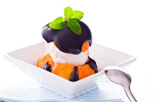 Profiterole in a small bowl with ice cream chocolate sauce and mint leaf on a white backgound