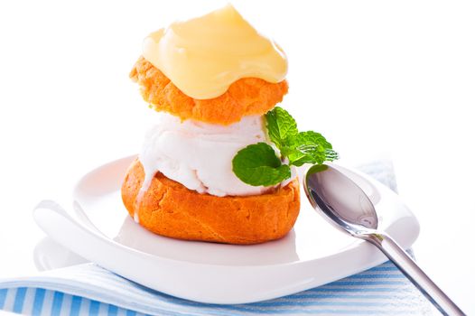 Profiterole in a small plate with ice cream vanilla sauce and mint leaf on a white backgound