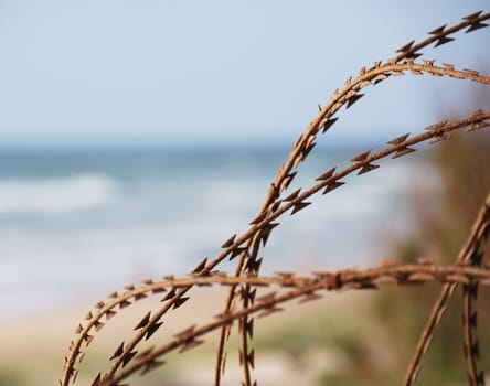 Border fence of rusty barbed wire on blurred blue sea background 