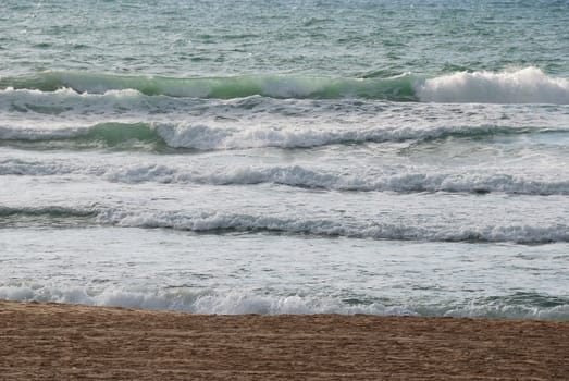 Sea coast with small waves and white horses formed by  foam 