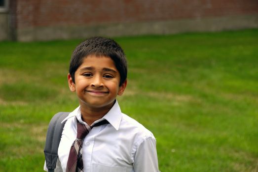 A happy Indian school kid smiling in front of the classroom
