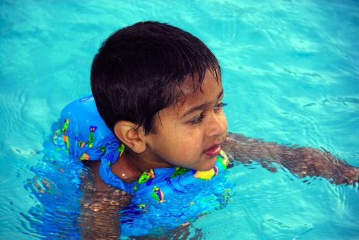 An young indian boy having fun smimming in the pool