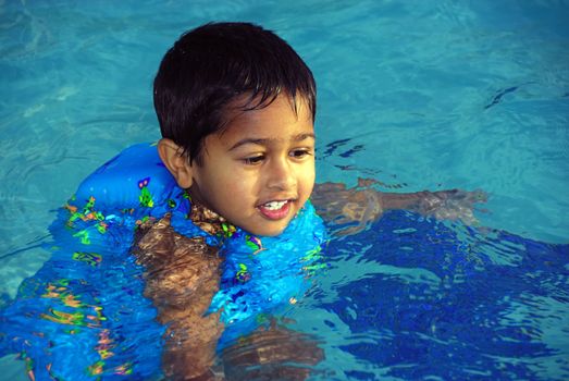 An young indian boy having fun smimming in the pool