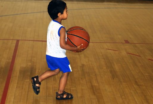 An young Indian kid playing with an old basket ball