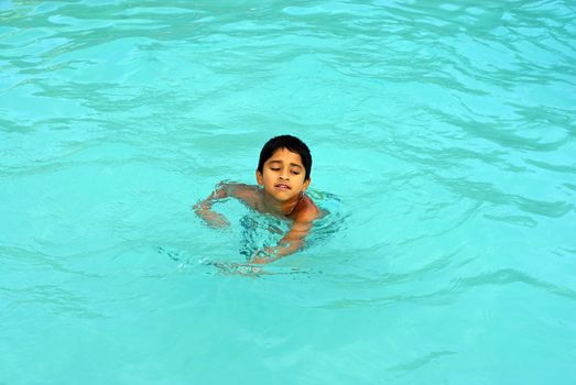 An young indian boy having fun smimming in the pool