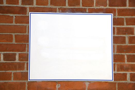 A blank white sign board against a brick wall ready for your text