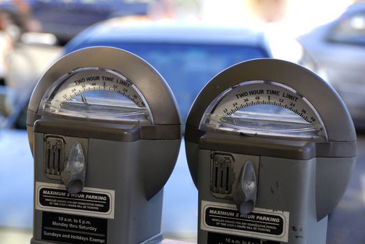 PArking meters againt a shallow depth of cars parked at the background