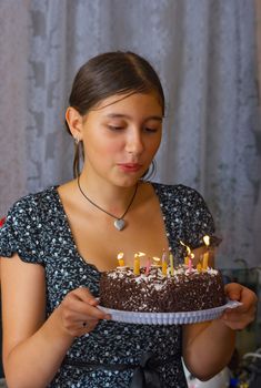 The happy girl blows into candles on a celebratory cake