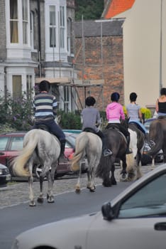 Group of girls riding on horse back between the cars.
