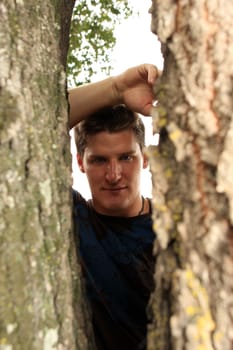 A man peering through the trunk of a tree