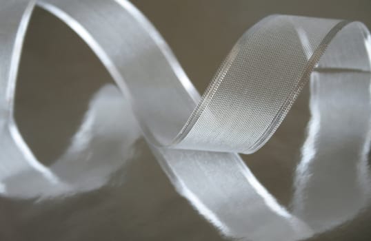 A piece of silver ribbon curled up on a metallic silver background. Shallow depth of field and selective focus.