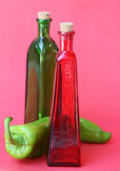 Glass bottle with a cork in the top and a large pepper in between. Shot against a red background