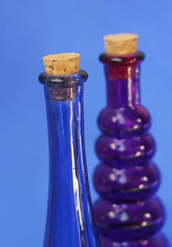 Empty blue and purple glass bottle with corks in the tops. Shot against a blue background