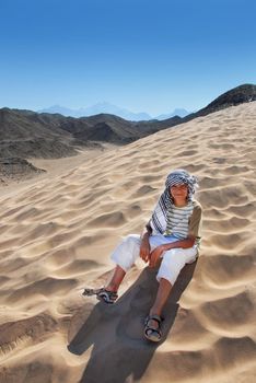 teenage smiling caucasian boy tourist sitting on sand dune in Egypt