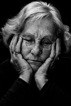 In a dark place: Dramatic exagerated low key portrait of an elderly woman looking very depressed and alone.