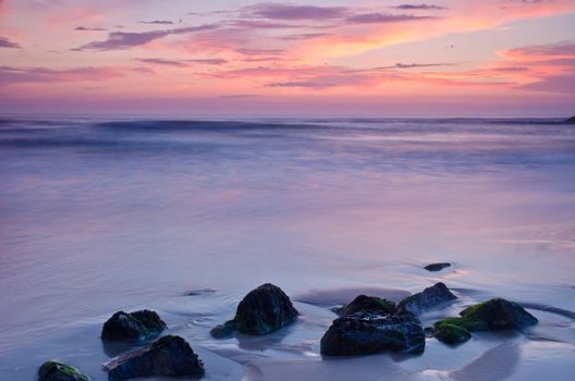 Sunset on a beach, beautiful sky and silky water arround rocks.