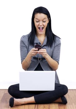Modern student life: Young woman happy or surprised while reading and texting on her cell phone with white laptop computer on her crossed legs.