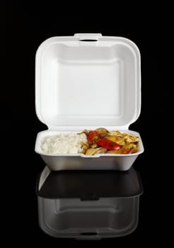 Chinese take-away food: Chicken with tomatoes, green onion, onions and potatoes accompanied by white rice in a styrofoam box photographed on black 