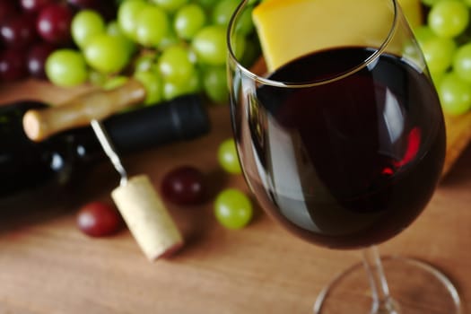 Red wine in wine glass with grapes, cheese a wine bottle and a corkscrew with cork in the background (Selective Focus, Focus on the front of the rim of the wine glass)